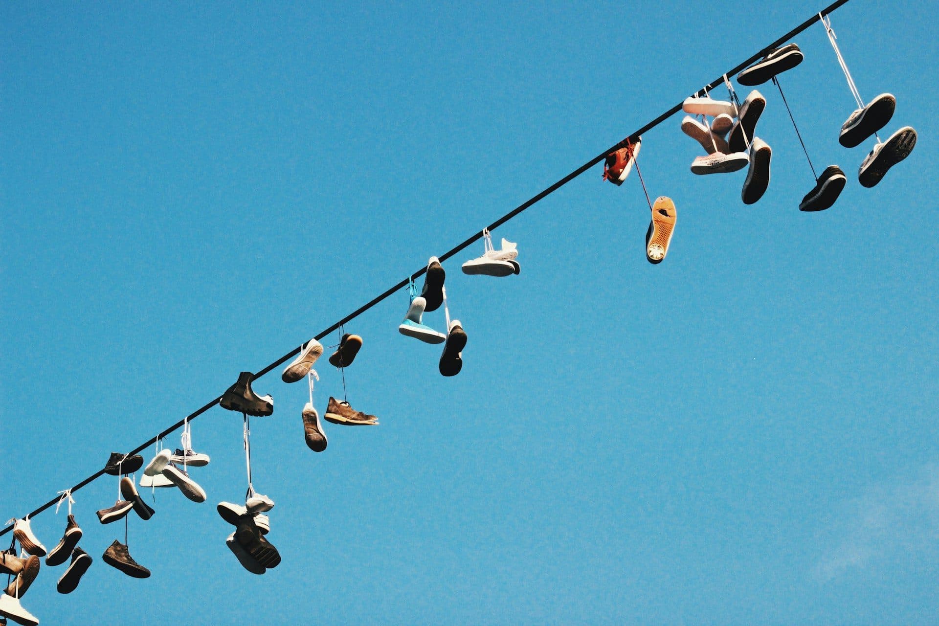 Dozens of different shoes hanging by their laces from a single wire against a clear blue sky