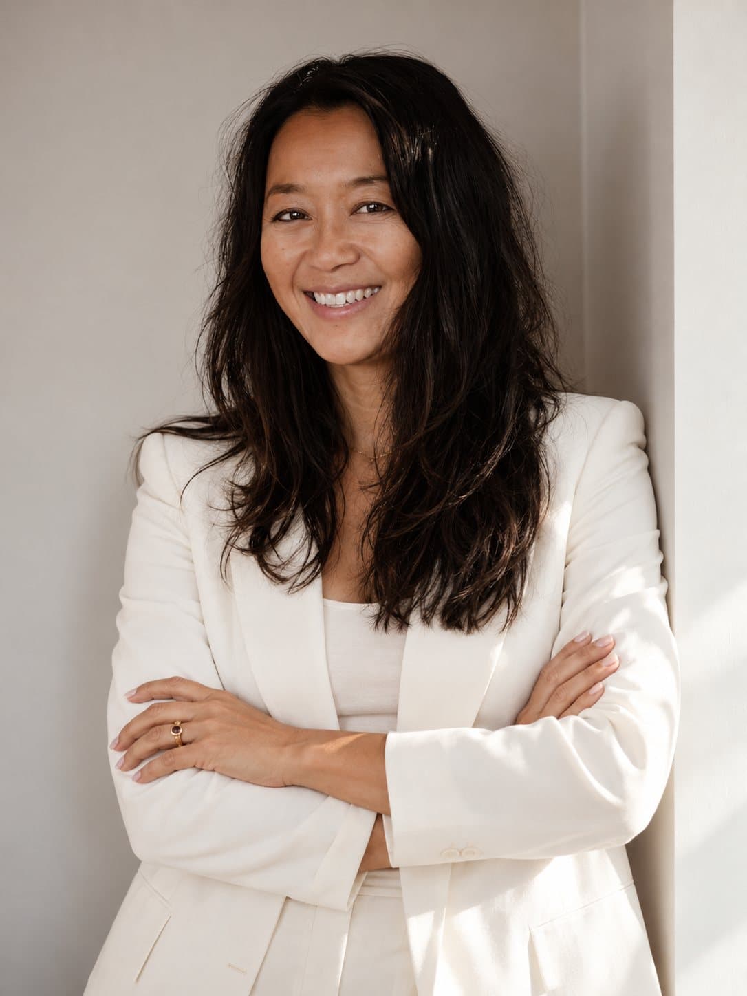 Anne Marie Mondrup smiling with arms crossed, in a cream blazer against a light wall